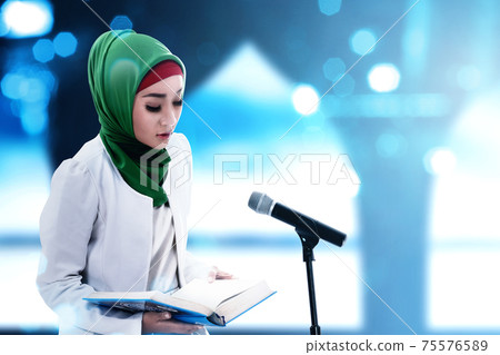 Asian Muslim woman in a veil sitting and reading the Quran Asian Muslim woman in a veil sitting and reading the Quran 75576589
