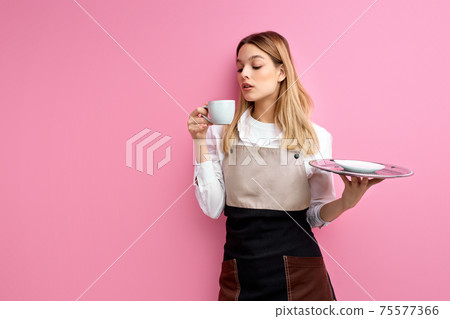 adorable caucasian waitress enjoying hot coffee isolated over pink studio background adorable caucasian waitress enjoying hot coffee isolated over pink studio background 75577366