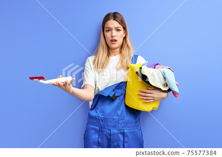 Young shocked woman holding bucket with group of cleaning supplies 75577384
