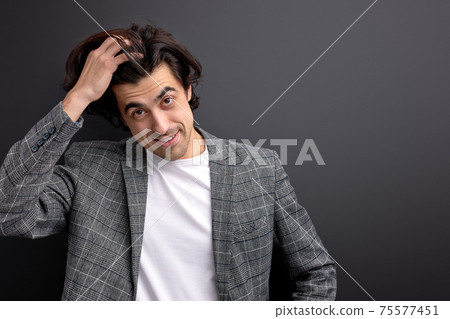 glad millennial guy in beautiful wear suit looking at camera touching hair glad millennial guy in beautiful wear suit looking at camera touching hair 75577451