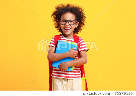 Happy schoolkid laughs at camera standing in studio with copybooks in hands Happy schoolkid laughs at camera standing in studio with copybooks in hands 75579156