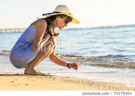 Young woman in summer clothes writing something on sand of sea beach. 75579365