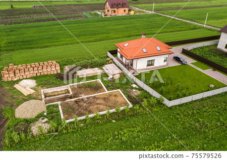 Aerial view of building site for future brick house, concrete foundation floor and stacks of yellow clay bricks for construction. Aerial view of building site for future brick house, concrete foundation floor and stacks of yellow clay bricks for construction. 75579526
