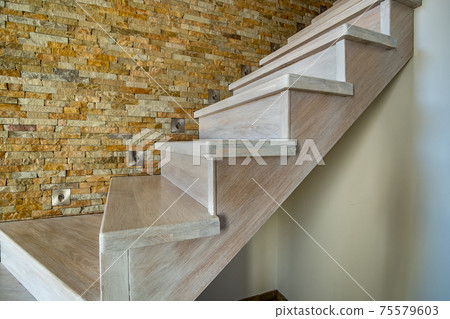 Stylish wooden contemporary staircase inside loft house interior. Modern hallway with decorative limestone brick walls and white oak stairs. 75579603