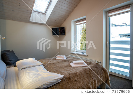 Interior of a spacious hotel bedroom on attic floor with fresh linen on a big double bed. Cozy contemporary mansard room in a modern house. Interior of a spacious hotel bedroom on attic floor with fresh linen on a big double bed. Cozy contemporary mansard room in a modern house. 75579606