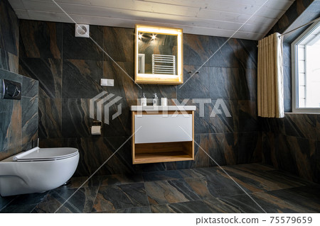Interior of modern stylish bathroom with black tiled walls, curtain shower place and wooden furniture with wash basin and big illuminated mirror. 75579659