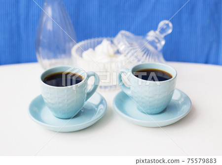 Two blue coffee cup on the table with a vase and saucer with marshmallows Two blue coffee cup on the table with a vase and saucer with marshmallows 75579883