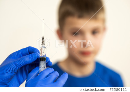 Doctor preparing vaccination injection with a syringe to an afraid child boy. Vaccination of children at school concept. Doctor preparing vaccination injection with a syringe to an afraid child boy. Vaccination of children at school concept. 75580111