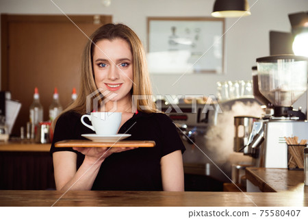 Beautiful female barista is working in coffee shop. Attractive woman is standing behind the bar Beautiful female barista is working in coffee shop. Attractive woman is standing behind the bar 75580407