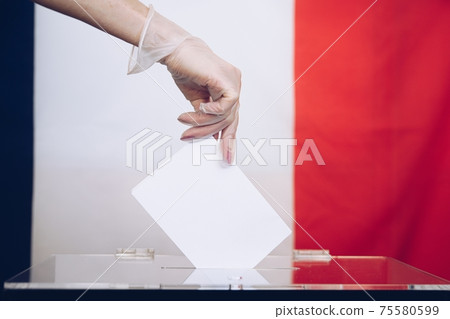 Woman's hand in medical glove throwing her vote into the ballot box. 75580599