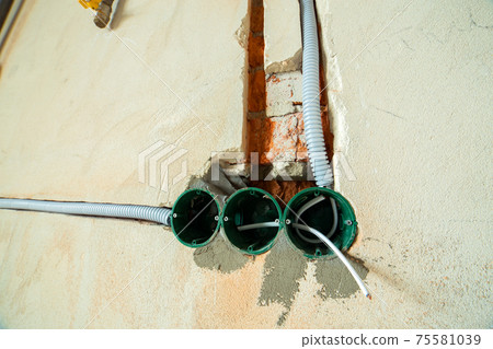 New electrical wiring installation, plastic boxes and electrical cables for future outlet sockets on the wall, renovation concept. New electrical wiring installation, plastic boxes and electrical cables for future outlet sockets on the wall, renovation concept. 75581039