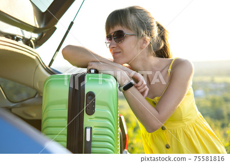 Young female driver having rest leaning on a green suitcase near her car in summer nature. Travel and vacations concept. 75581816