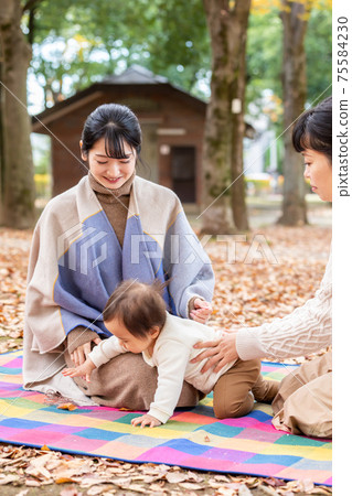 A woman hugging her baby in the park and talking to her mommy friend A woman hugging her baby in the park and talking to her mommy friend 75584230