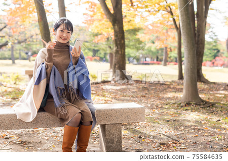 Woman with a smartphone in the autumn park Woman with a smartphone in the autumn park 75584635