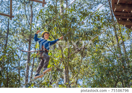 Happy child in a helmet, healthy teenager school boy enjoying activity in a climbing adventure park on a summer day 75586796