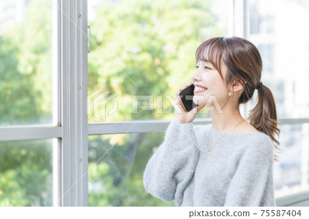 A woman by the window making a phone call Business scene A woman by the window making a phone call Business scene 75587404