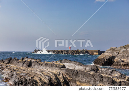 Red lighthouse on the breakwater of the harbor in the rocky area, the waves break due to strong winds Red lighthouse on the breakwater of the harbor in the rocky area, the waves break due to strong winds 75588677