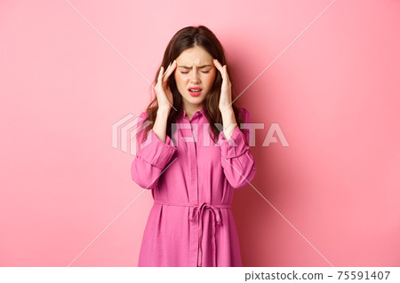 Woman feeling pain in head, touching temples and frowning, suffering migraine, being dizzy, standing with headache against pink background 75591407