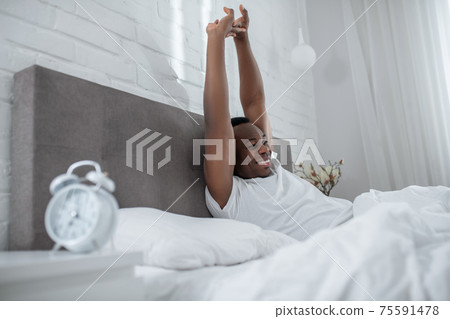 A young man in white tshirt lying in bed and looking sleepy 75591478
