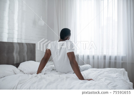African american man sitting on bed and stretching African american man sitting on bed and stretching 75591655