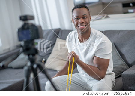 African american young man showing exercises with elastic band African american young man showing exercises with elastic band 75591684