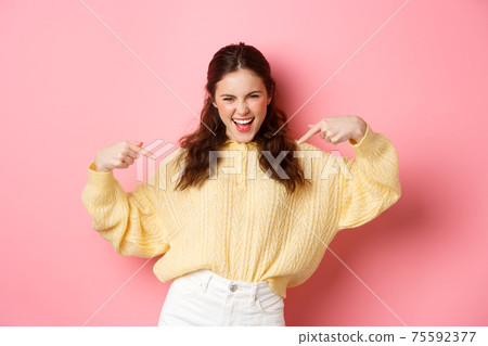 Young attractive woman dancing and pointing at herself, pick or choose me gesture, self-promoting personal abilities, standing against pink background Young attractive woman dancing and pointing at herself, pick or choose me gesture, self-promoting personal abilities, standing against pink background 75592377