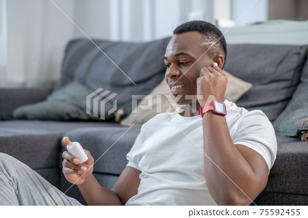 African american guy in white clothes wearing wireless earphone African american guy in white clothes wearing wireless earphone 75592455