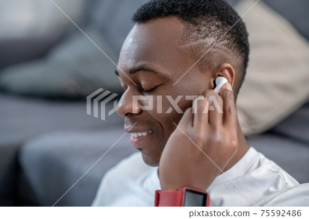 African american guy in white clothes wearing wireless earphone African american guy in white clothes wearing wireless earphone 75592486