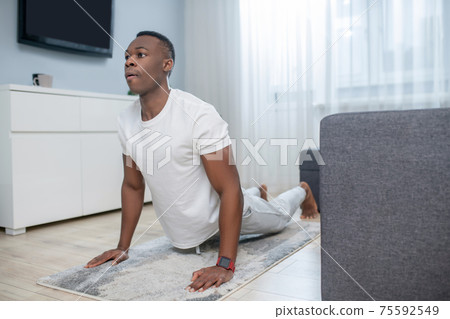African american guy in white clothes having ahome workout African american guy in white clothes having ahome workout 75592549