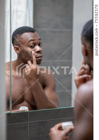 African american short-haired guy applying some cream on his face African american short-haired guy applying some cream on his face 75592578