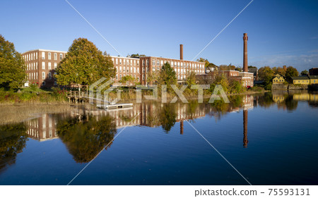 A 19th century textile mill has been renovated for modern use, seen reflected in the neighboring 75593131