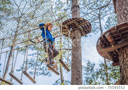 Happy child in a helmet, healthy teenager school boy enjoying activity in a climbing adventure park on a summer day 75593552