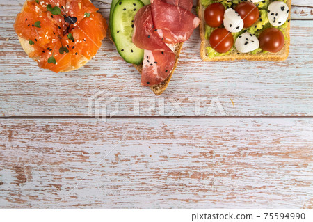 An assortment of sandwiches with fish, cheese, meat and vegetables lay on the wooden table 75594990