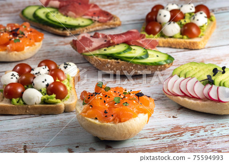An assortment of sandwiches with fish, cheese, meat and vegetables lay on the wooden table 75594993