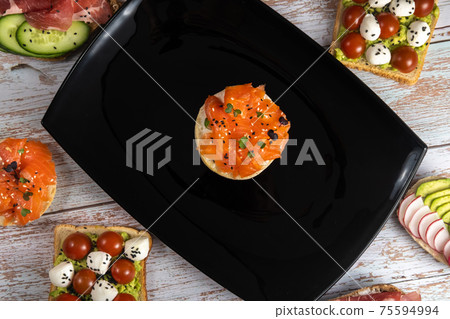 A red fish sandwich is on a black plate and there are many other sandwiches around 75594994
