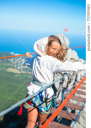 Girls crossing the chasm on the rope bridge. Girls crossing the chasm on the rope bridge. 75595063