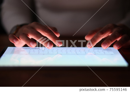 Female fingers are typing on tablet screen at night Female fingers are typing on tablet screen at night 75595146