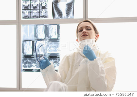 Tired doctor in protective suit sits on floor with X-rays hanging in background Tired doctor in protective suit sits on floor with X-rays hanging in background 75595147