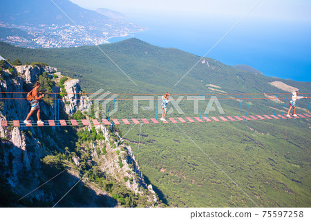 Family crossing the chasm on the rope bridge. Black sea background, Crimea, Russia Family crossing the chasm on the rope bridge. Black sea background, Crimea, Russia 75597258