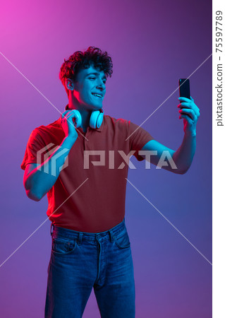 Young man in headphones isolated on gradient background in neon light Young man in headphones isolated on gradient background in neon light 75597789