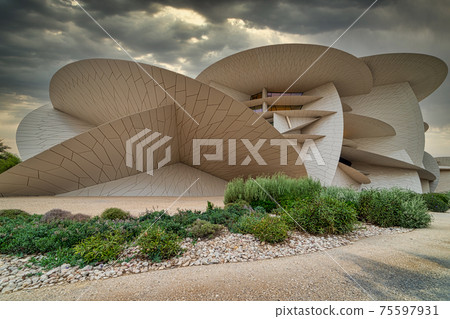 National Museum of Qatar (Desert rose) panoramic external view at sunset with clouds in the sky in background 75597931