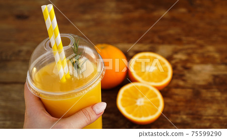 Girl hand is holding plastic glass with orange juice, wooden background. Girl hand is holding plastic glass with orange juice, wooden background. 75599290
