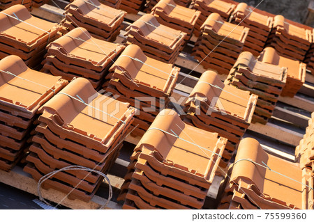 Stacks of yellow ceramic roofing tiles for covering residential building roof under construction. Stacks of yellow ceramic roofing tiles for covering residential building roof under construction. 75599360