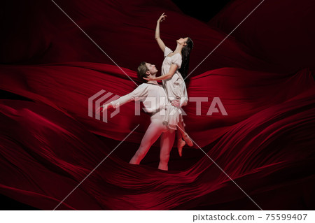 Young and graceful ballet dancers on billowing red cloth background in classic action. Art, motion, action, flexibility, inspiration concept. 75599407