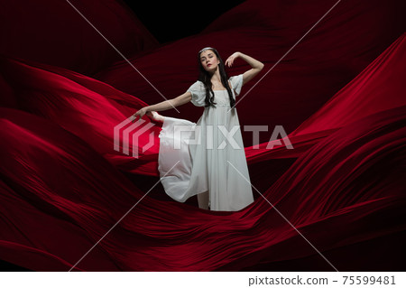 Young and graceful ballet dancer on billowing red cloth background in classic action. Art, motion, action, flexibility, inspiration concept. 75599481