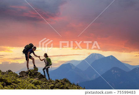 Tourist couple helping each other to climb high rock in evening mountains at sunset. Tourist couple helping each other to climb high rock in evening mountains at sunset. 75599483