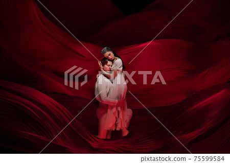 Young and graceful ballet dancers on billowing red cloth background in classic action. Art, motion, action, flexibility, inspiration concept. Young and graceful ballet dancers on billowing red cloth background in classic action. Art, motion, action, flexibility, inspiration concept. 75599584