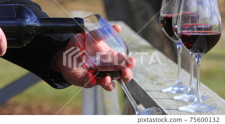 Man hand pouring red wine from the bottle into glasses with friends outside Man hand pouring red wine from the bottle into glasses with friends outside 75600132