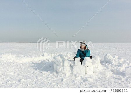 Happy woman building an igloo on the snow Happy woman building an igloo on the snow 75600321