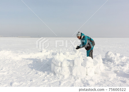 Happy woman building an igloo on the snow Happy woman building an igloo on the snow 75600322